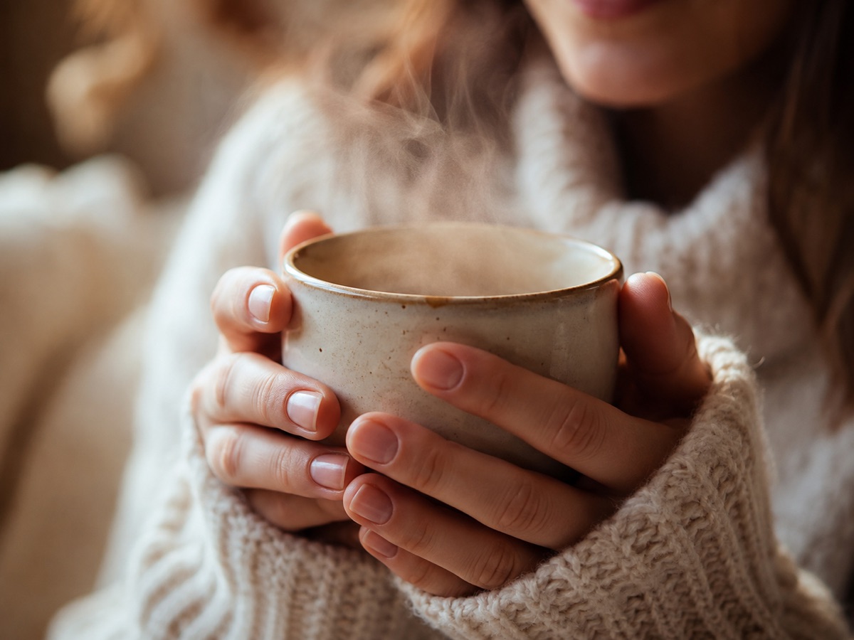 Person hält eine dampfende Tasse mit beiden Händen